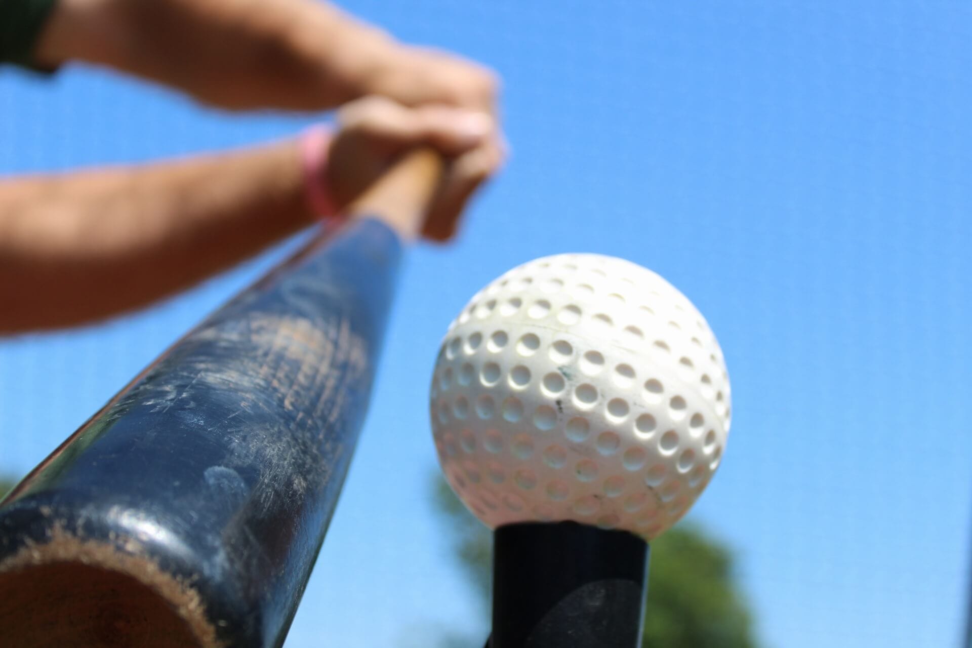Man hitting dimpled white baseball with baseball bat