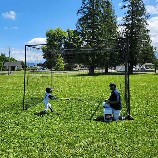 Man soft tossing a ball to youth player while he hits it into the BCI Backstop
