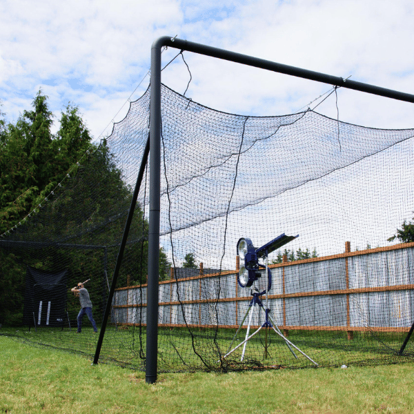 Iron Horse batting cage in a backyard with a man batting baseballs from a bata 2 pitching machine
