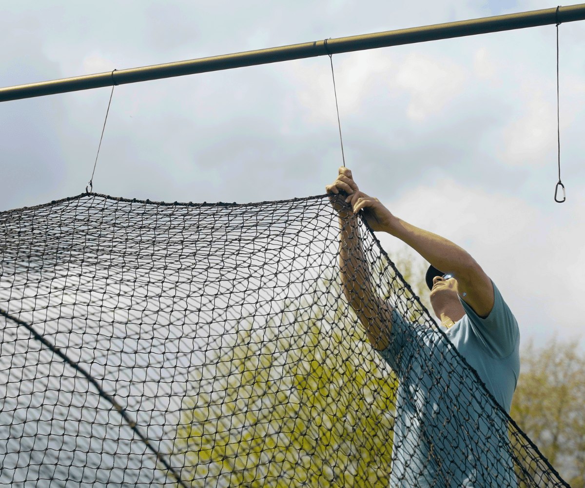 Man hanging batting cage net to batting cage frame with clips