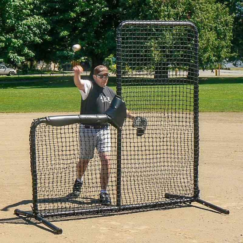 A person practices hitting inside the 10-Foot Wide Batting Cage System by BATTING CAGES INC, set up on a grassy lawn with durable HDPE netting; a small building and clear sky are visible in the background.