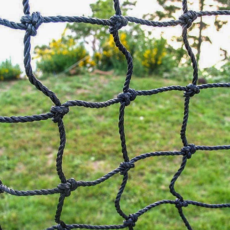 A person practices hitting inside the 10-Foot Wide Batting Cage System by BATTING CAGES INC, set up on a grassy lawn with durable HDPE netting; a small building and clear sky are visible in the background.