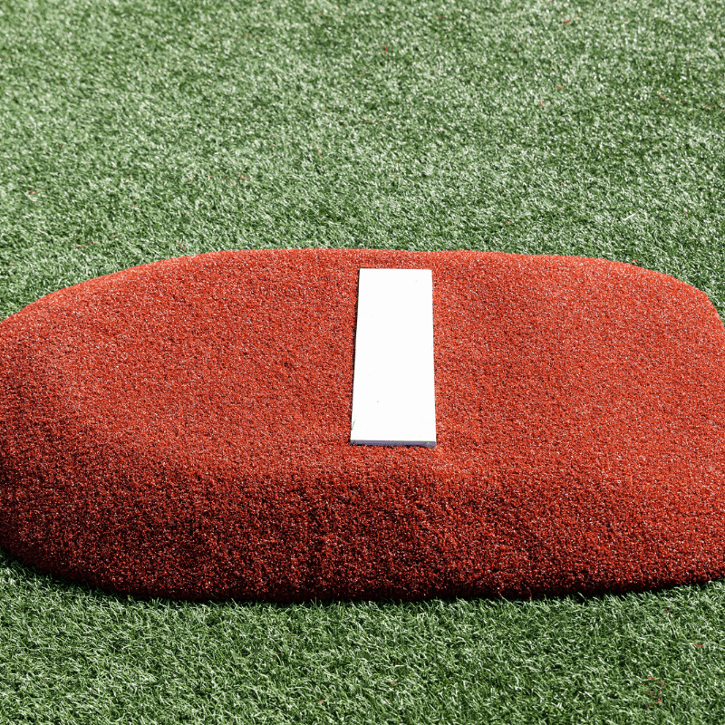 A child in red athletic shoes and striped pants stands on a PORTOLITE 4" Economy Youth Mound, surrounded by green artificial turf.