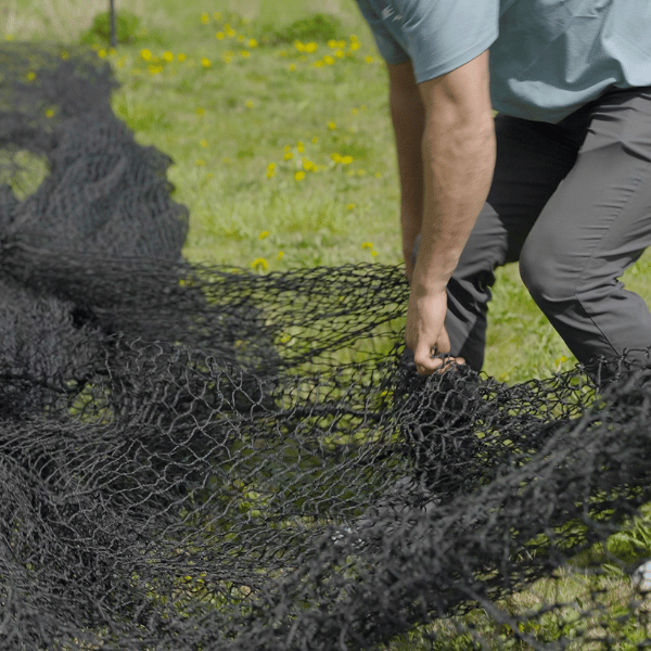 Man moving around a batting cage net 