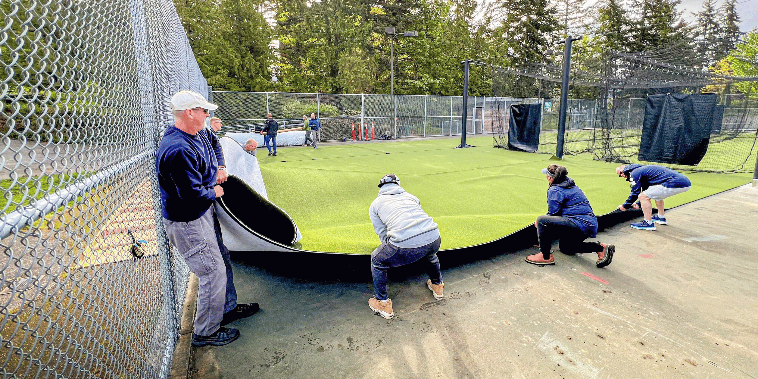 Men positioning batting cage turf 