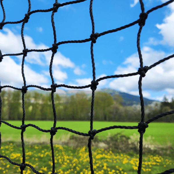 Flat panel netting hung up close with green grass, trees, and blue skies behind it