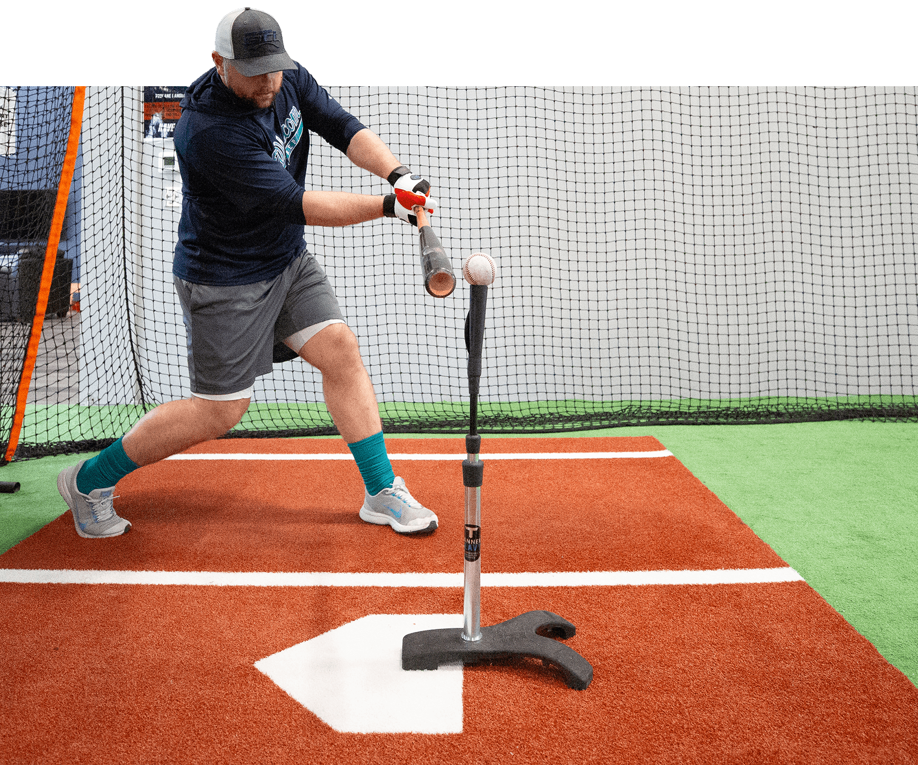 Man hitting baseball off of tanner heavy tee in indoor facility