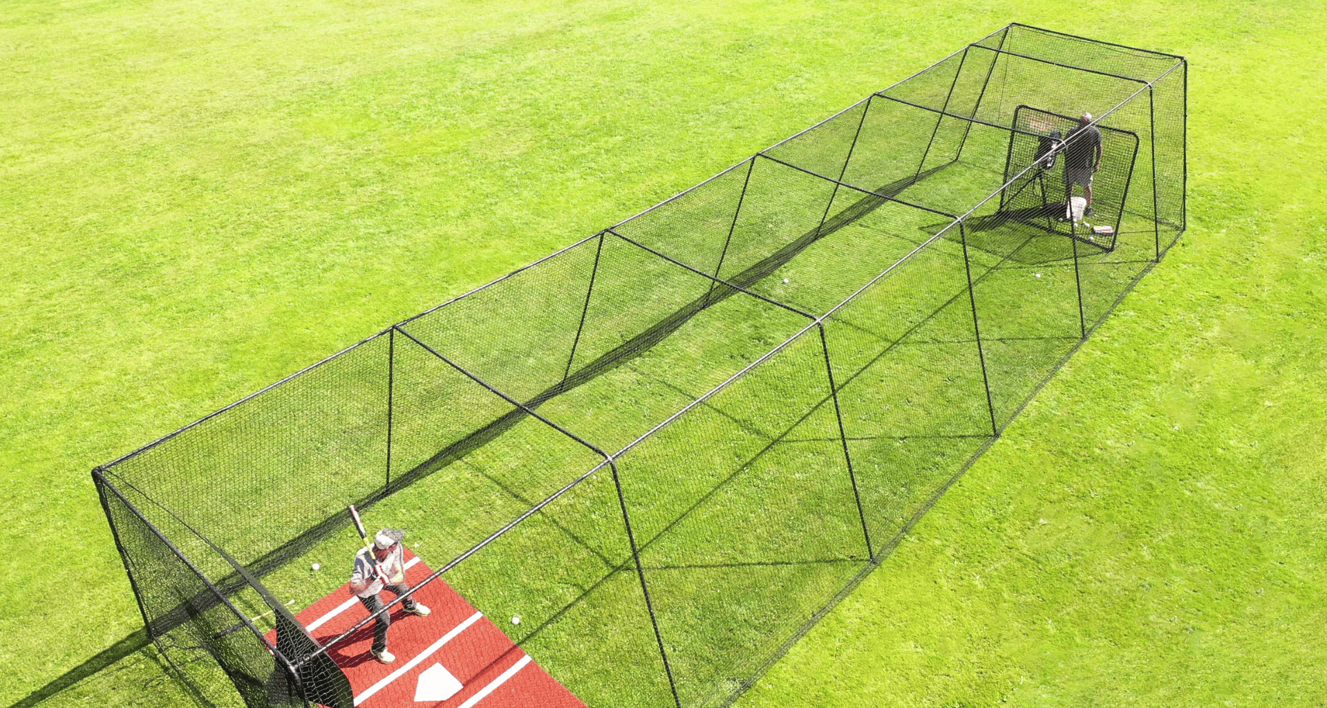 Man hitting baseballs inside of the Trapezoid batting cage