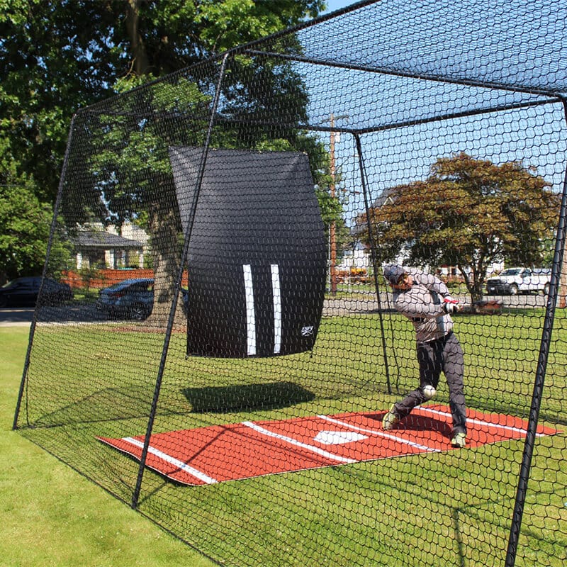 Man batting in the Freestanding Trapezoid Batting Cage with the clay batters box and vinyl backdrop behind him