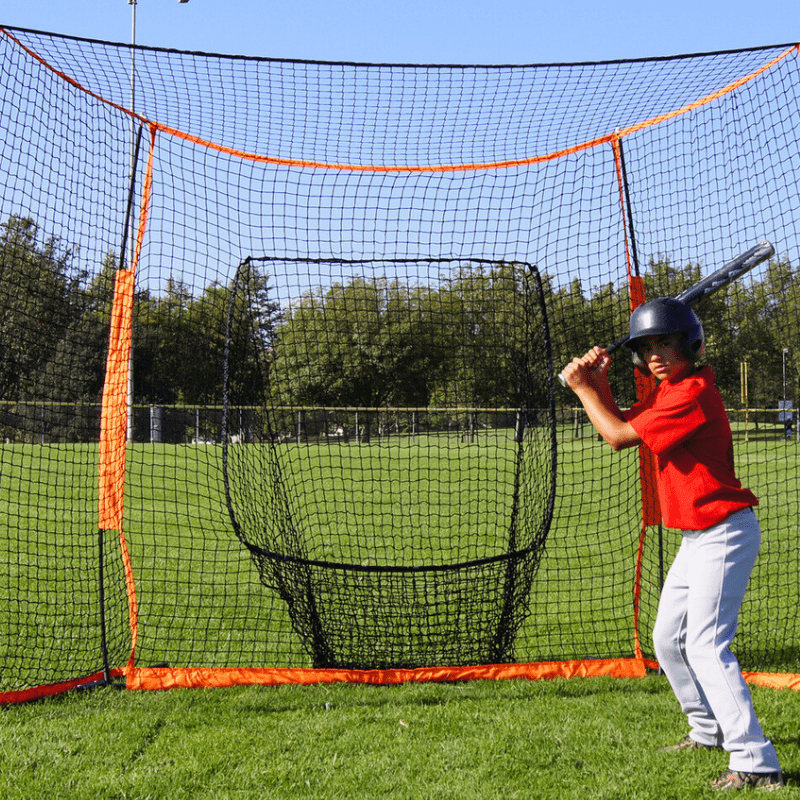 Kid hitting baseballs in front of the Bownet Portable Hitting Station  in park with green grass