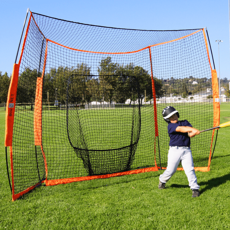 Kid hitting baseballs in front of the Bownet Portable Hitting Station  in park with green grass